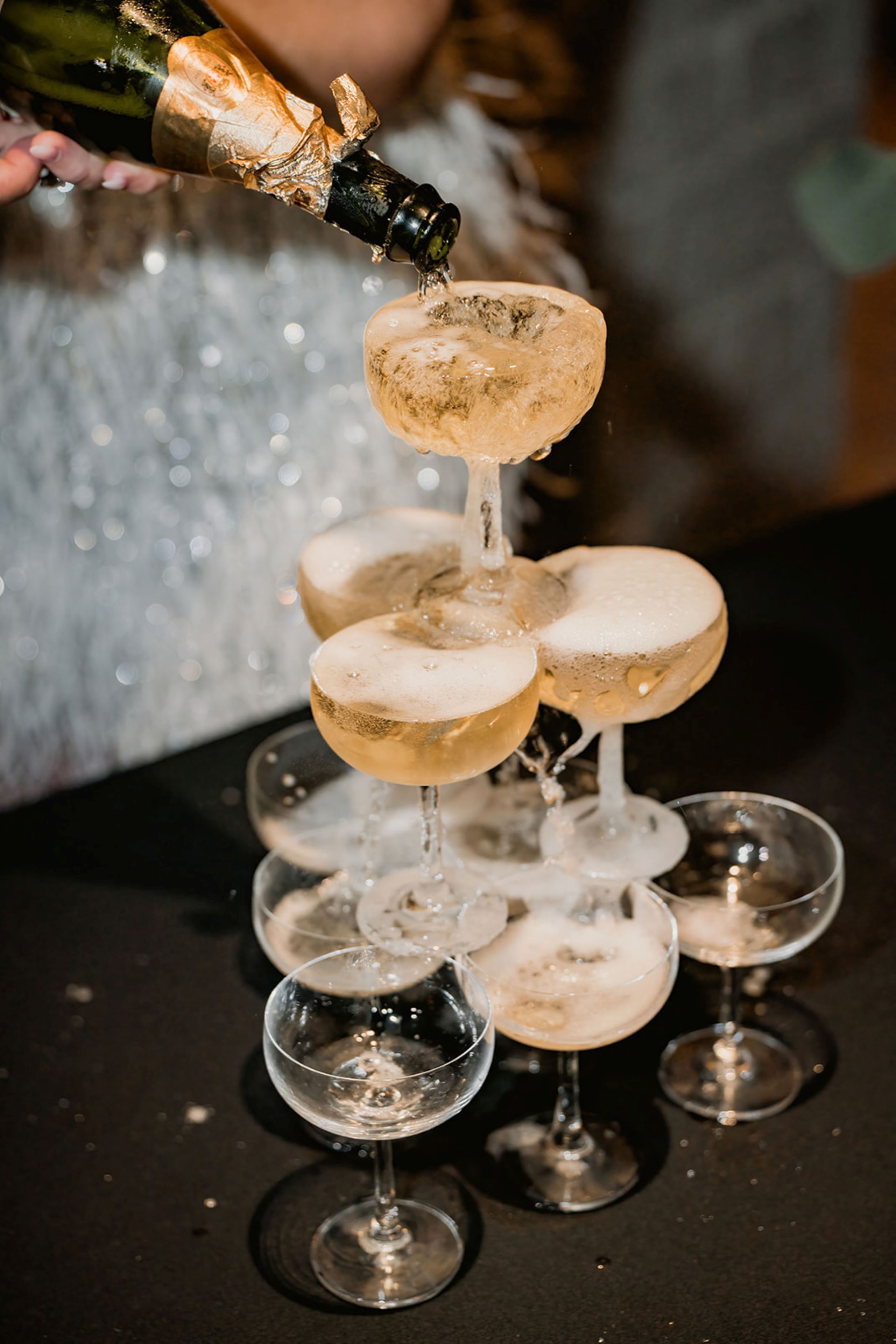 A champagne bottle being poured into a pyramid of champagne glasses.