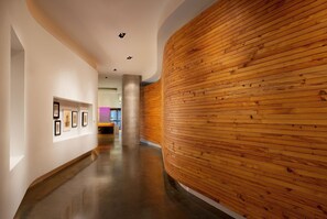 A hallway with a wooden wall and a concrete pillar, leading to a room with a purple-lit corner.