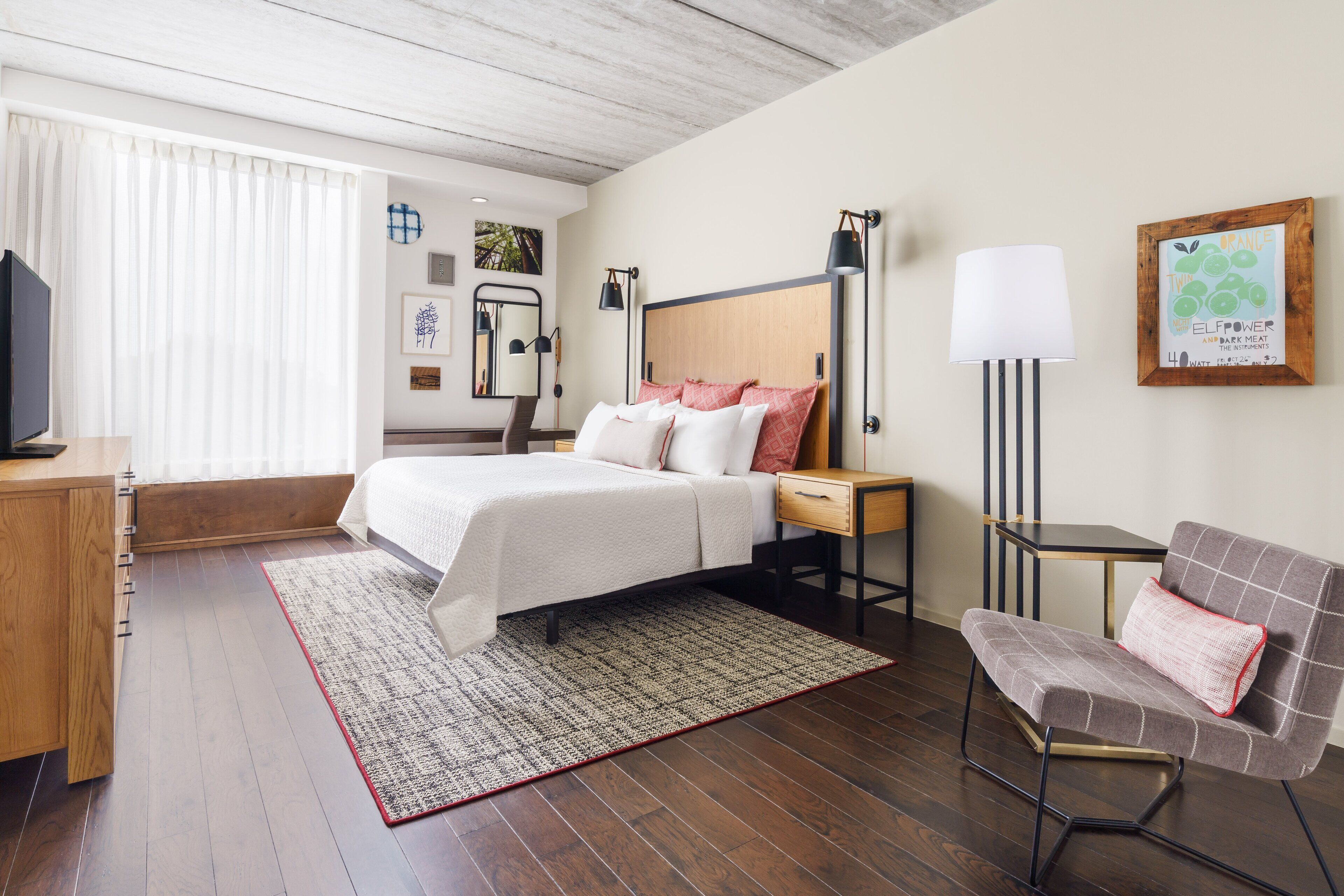 A hotel room with a bed, bedside table, lamp, chair, and a TV.