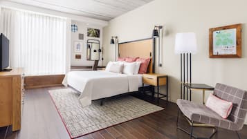 A hotel room with a bed, bedside table, lamp, chair, and a TV.