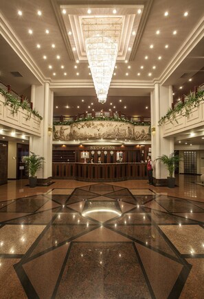 Un hall d’entrée spacieux, agrémenté d’un magnifique lustre, d’un comptoir de réception et d’un plafond élevé orné de moulures décoratives.