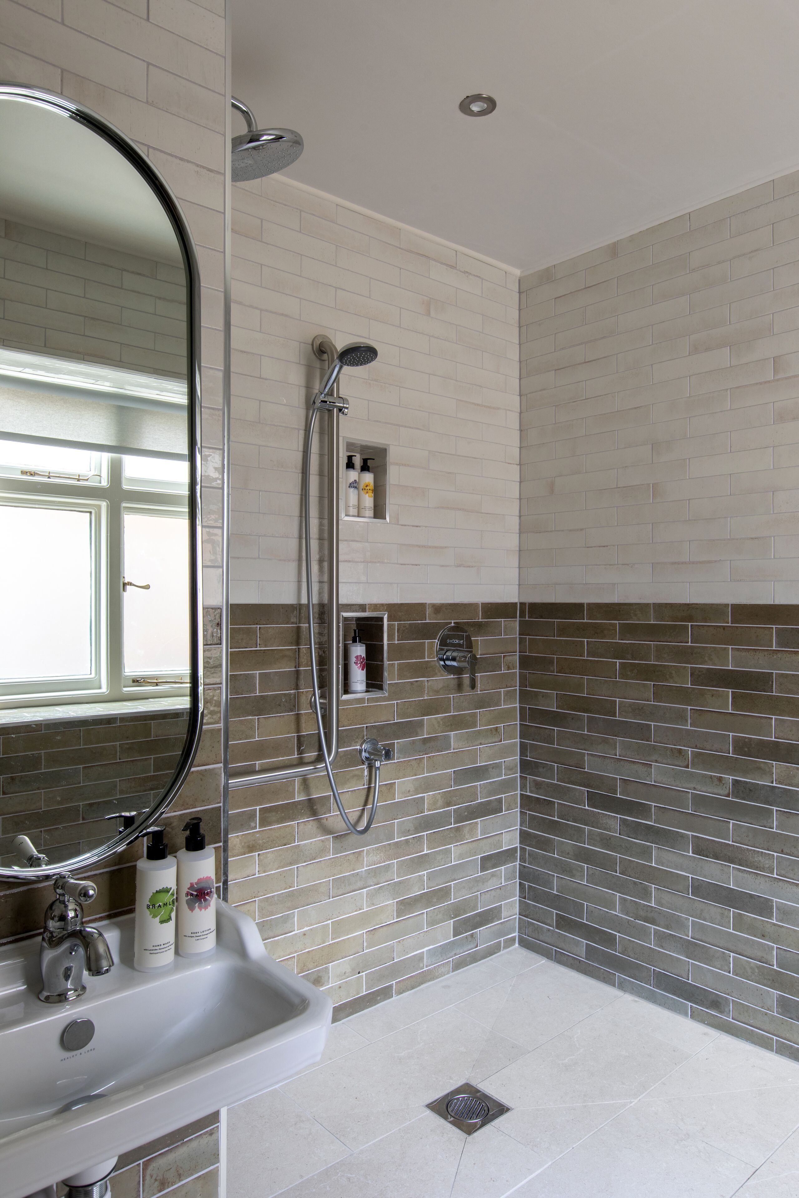 Un baño con un lavamanos blanco, un espejo, una ducha y una pared con azulejos.