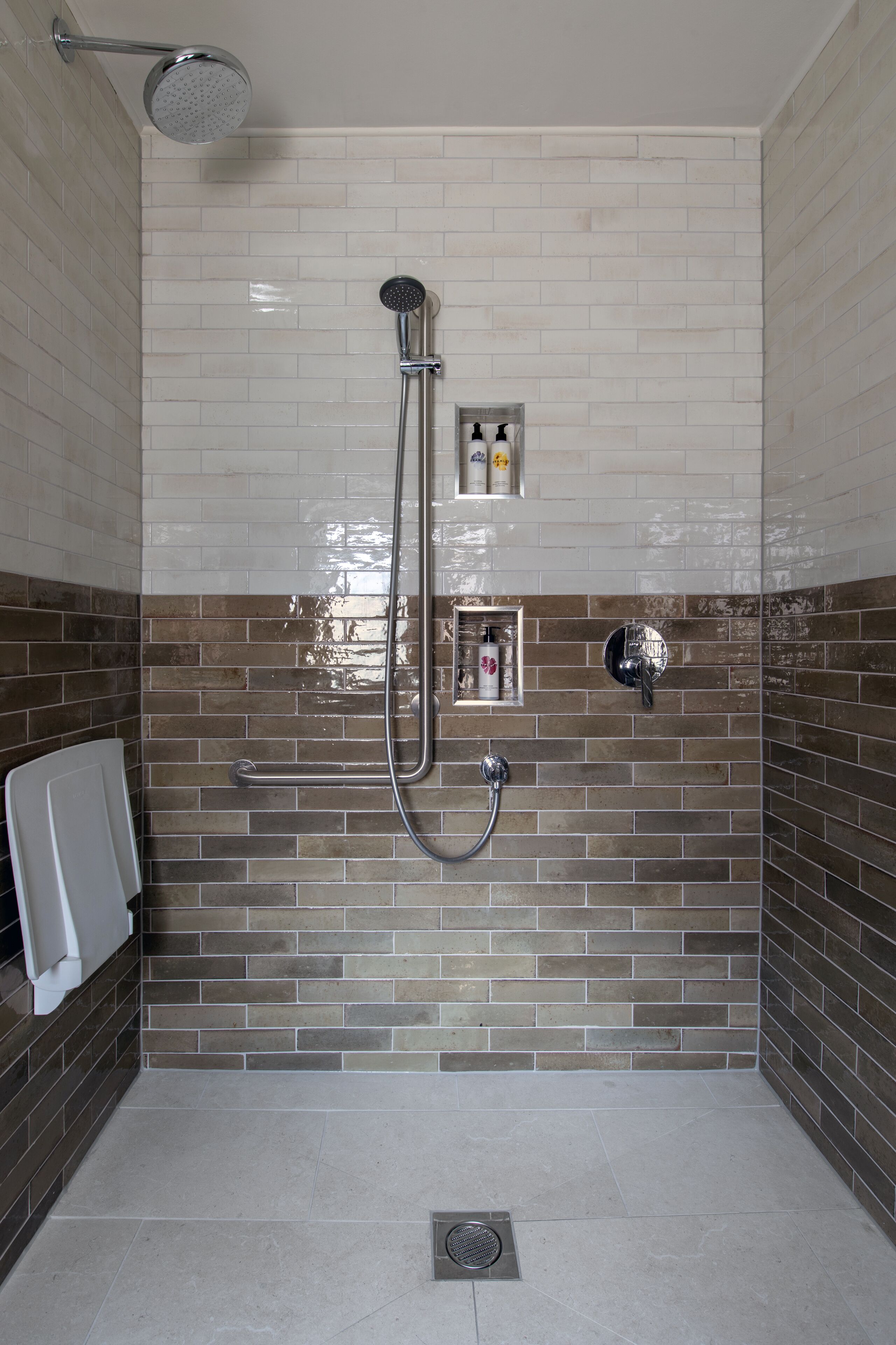 A shower area with a tiled wall, a handheld showerhead, a wall-mounted faucet, and a small shelf with toiletries.