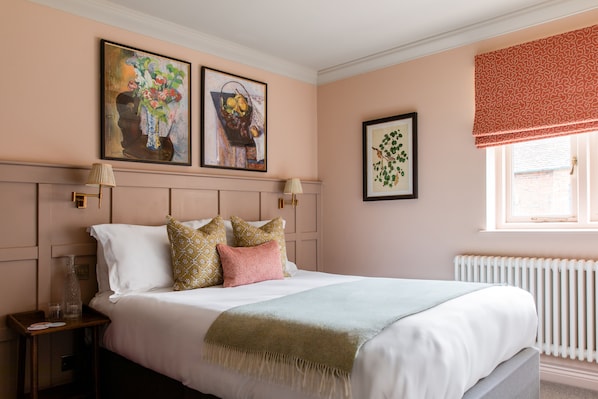 A neatly arranged bedroom with a bed, bedside tables, and artwork on the walls. - The Carnarvon Arms (Newbury)