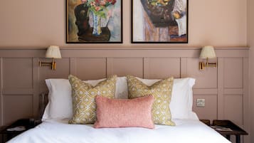 A hotel room with a bed, two wall-mounted lamps, and two framed paintings above the bed.