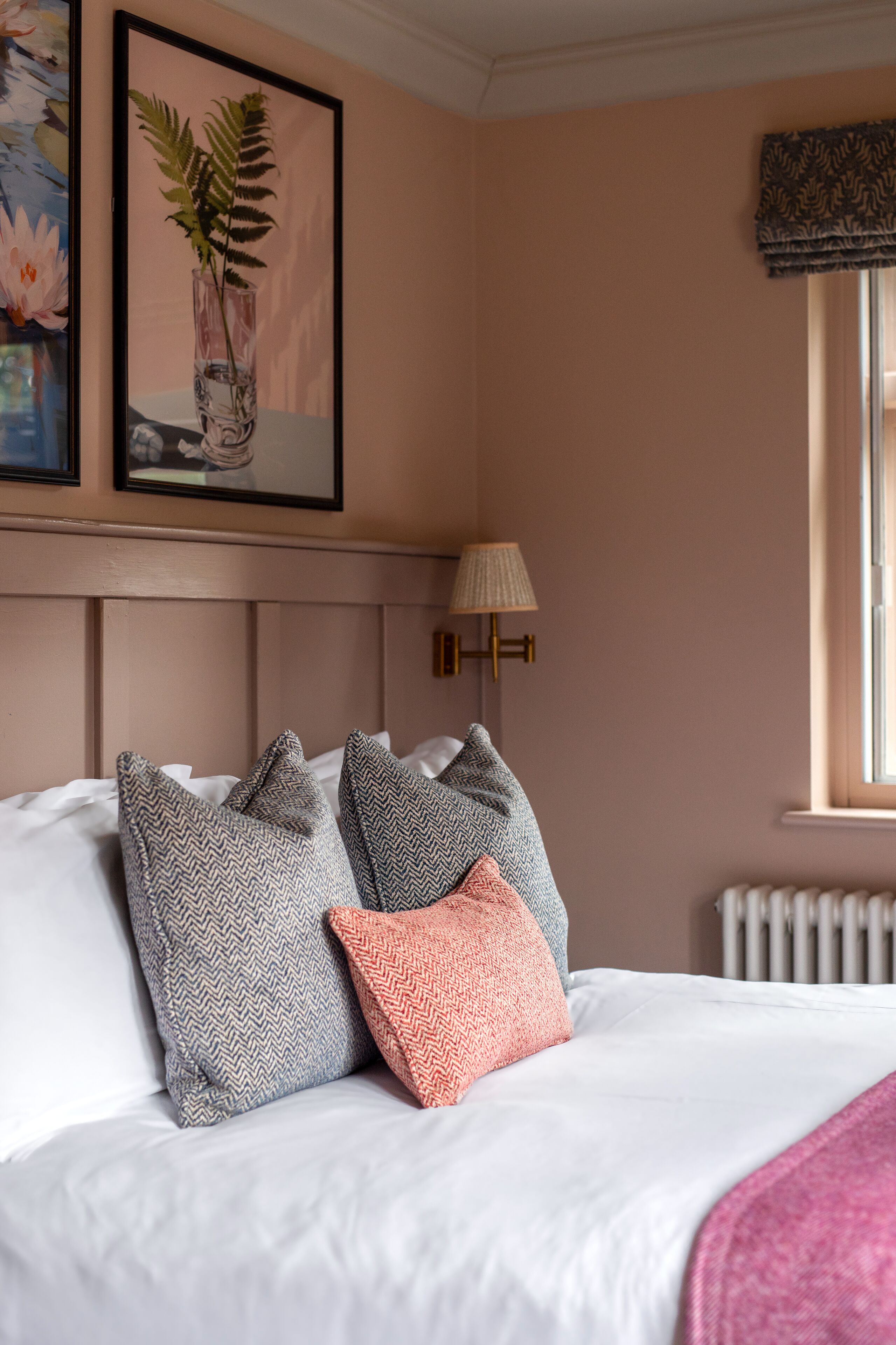 Un letto ben rifatto con cuscini decorati, un quadro appeso sopra e una lampada da comodino.