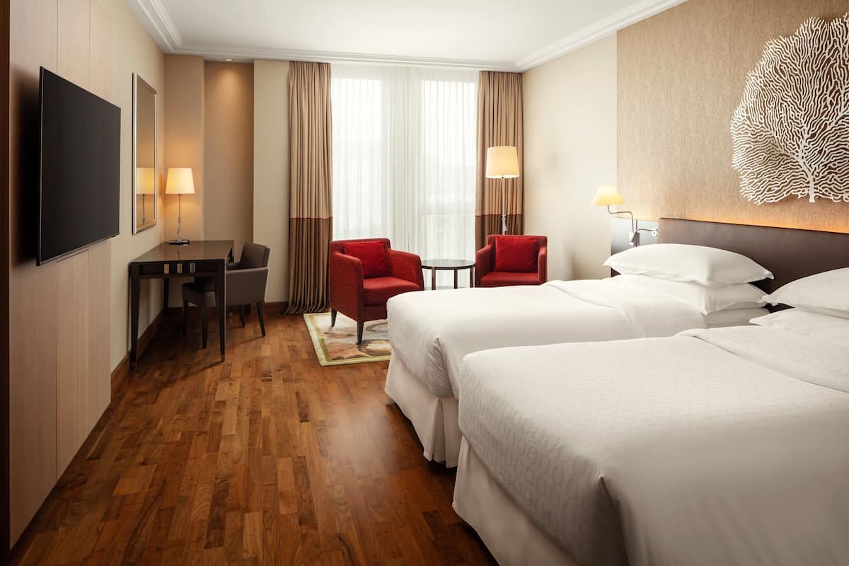 A hotel room with two beds, a desk with a chair, a TV, and a decorative wall piece.