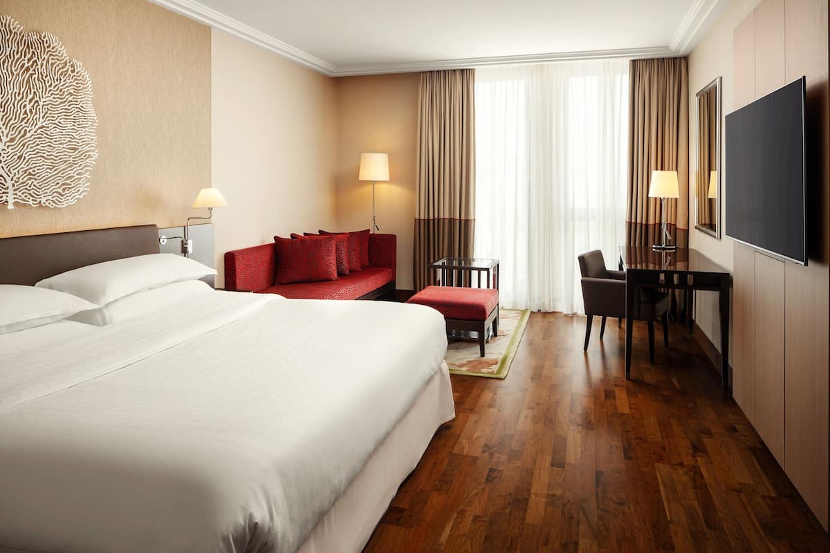A hotel room with a large bed, a red sofa, a desk with a chair, and a TV.