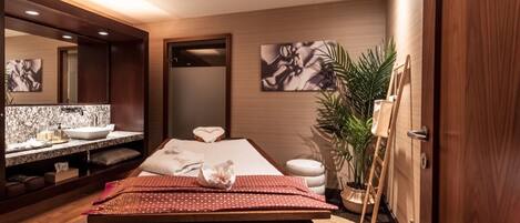 Een moderne spa-ruimte met een houten vloer, een massagetafel, een grote spiegel en een wastafel met een marmeren blad.