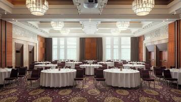Un salón de conferencias con varias mesas redondas y sillas, ventanas amplias y candelabros.