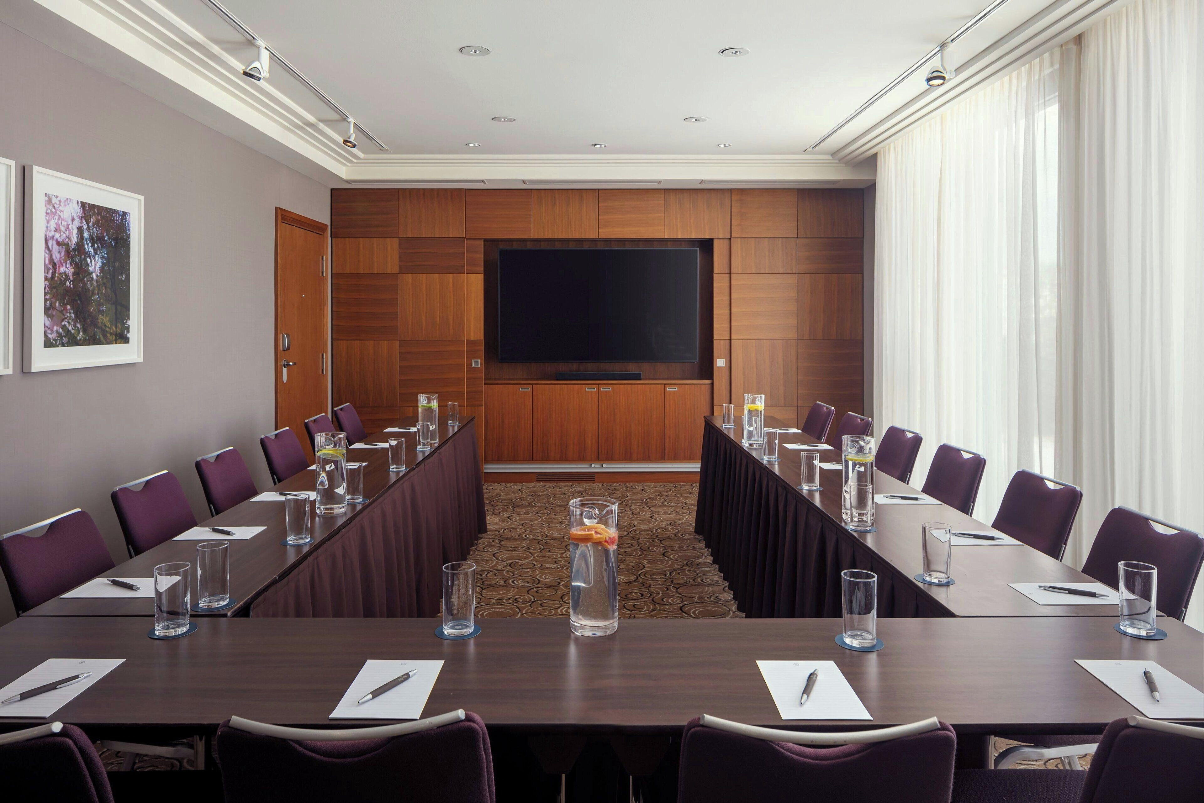 A conference room with a long table, chairs, a large screen, and a carpeted floor.