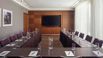 A conference room with a long table, chairs, a large screen, and a carpeted floor.