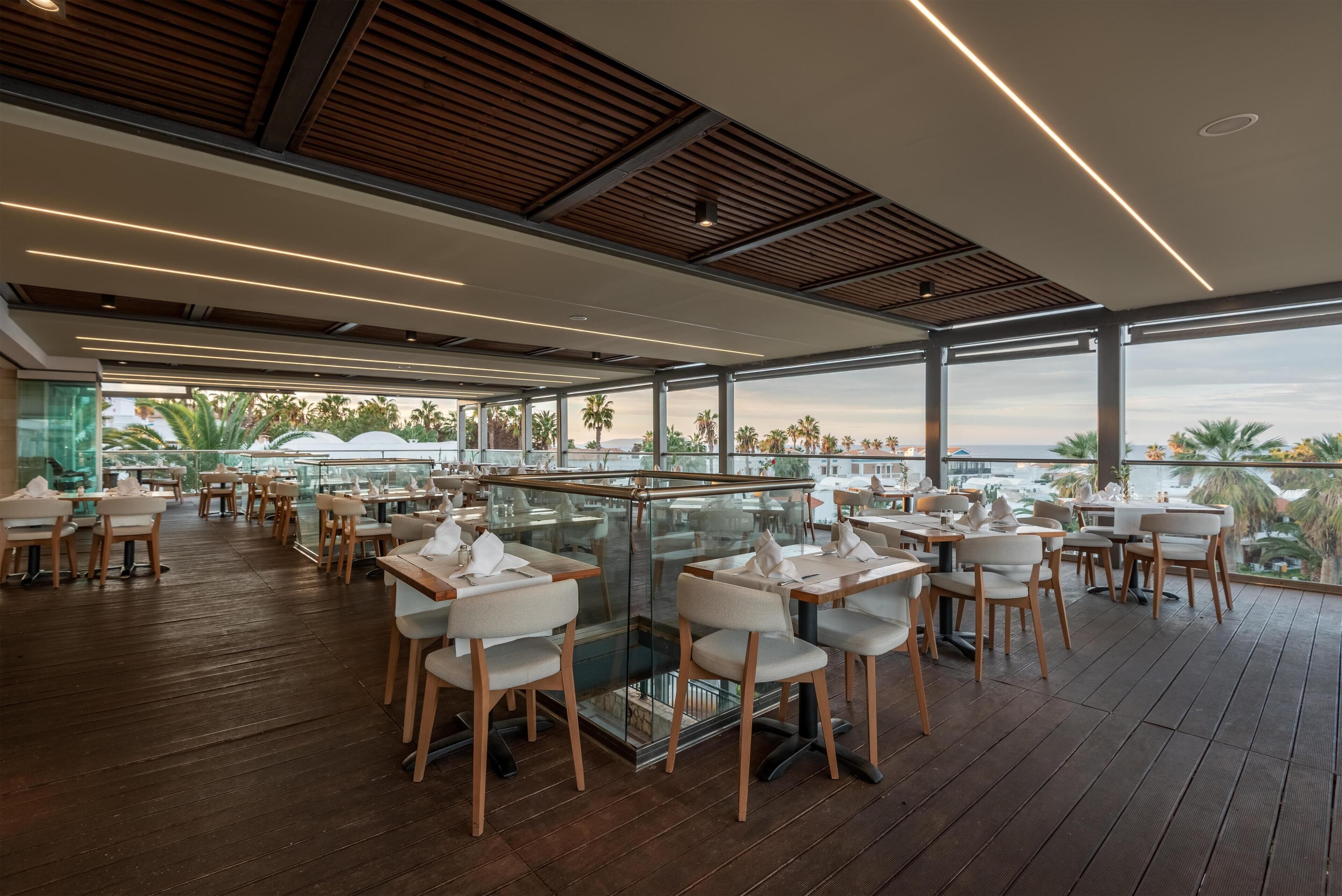 Un comedor interior con suelo de madera, barandillas de cristal y mesas dispuestas para comer.