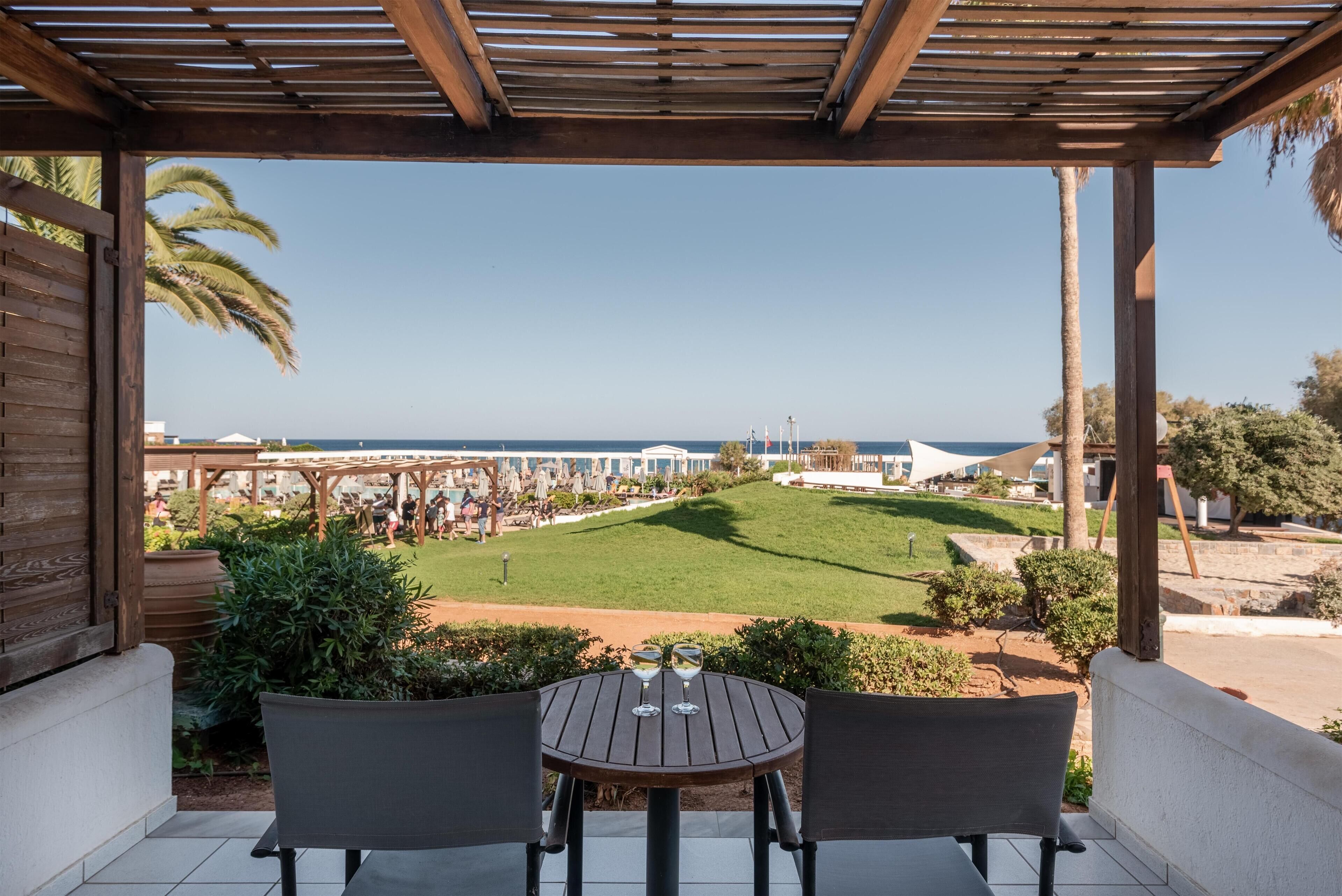A covered patio with a table and chairs, overlooking a well-maintained lawn and a view of the sea.
