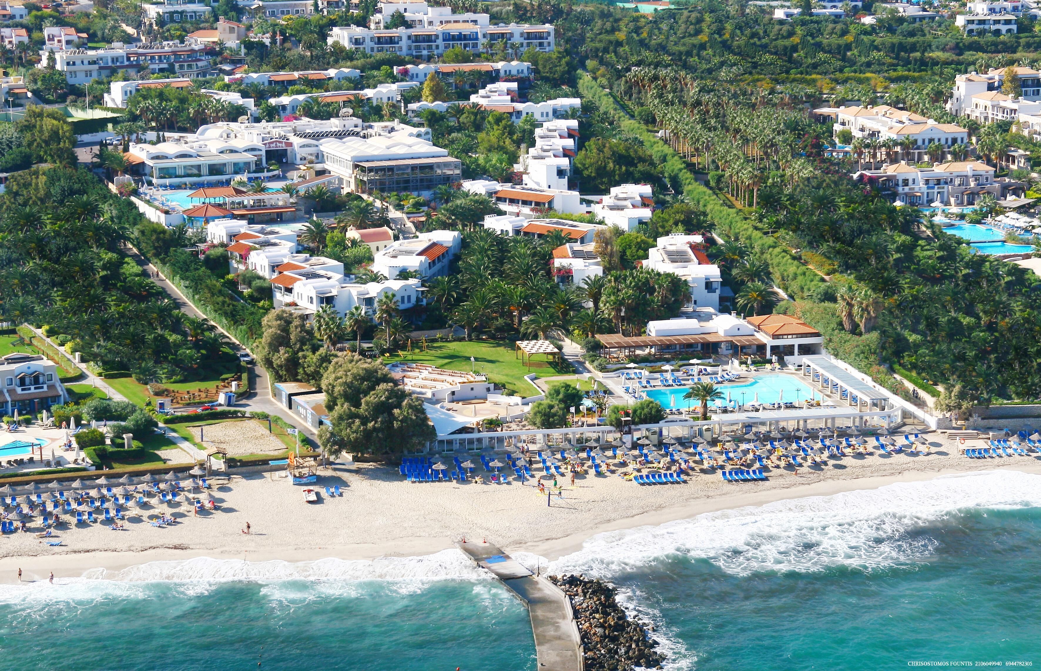 An aerial view of a coastal resort with multiple buildings, a beach, and a swimming pool.