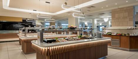 Un área de buffet moderna con múltiples mostradores de servicio, iluminación colgante y un piso de baldosas limpias.