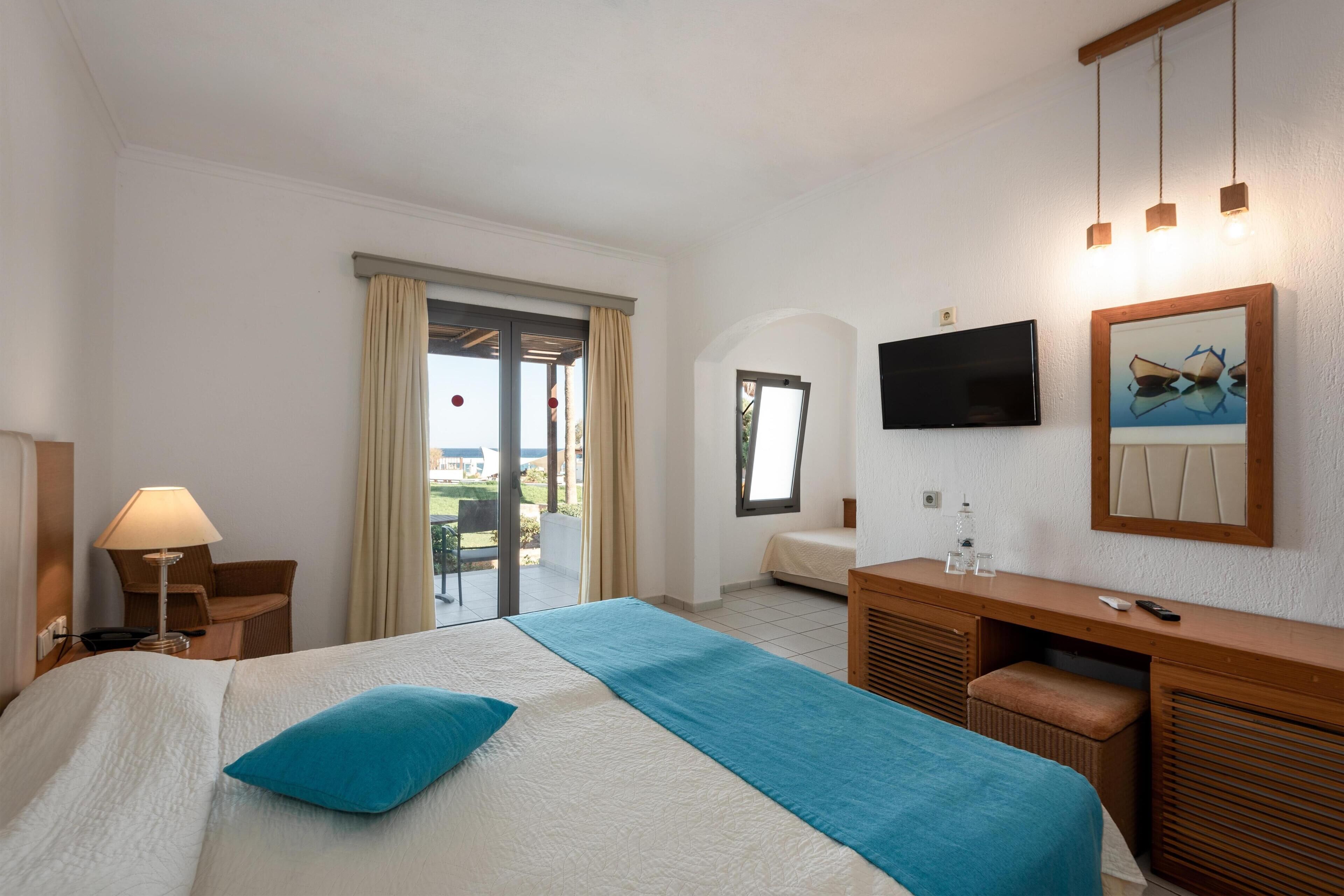 Hotelkamer met een bed, een bureau, een televisie en een balkon met gordijnen.