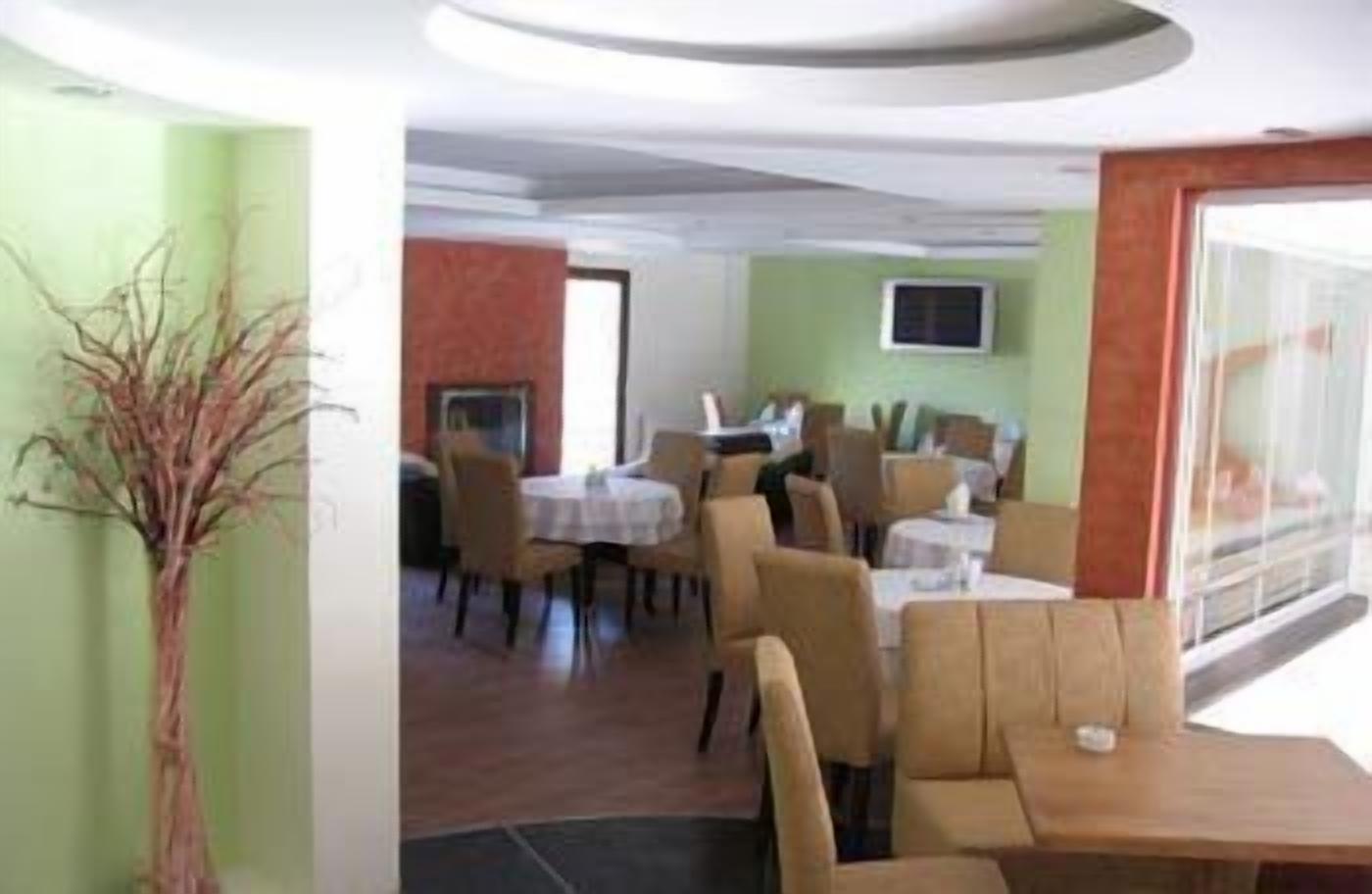 A restaurant with round tables and chairs, a flat-screen TV on the wall, and a large window providing a view of the outdoors.