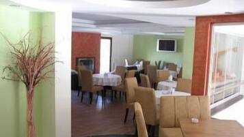 A restaurant with round tables and chairs, a flat-screen TV on the wall, and a large window providing a view of the outdoors.