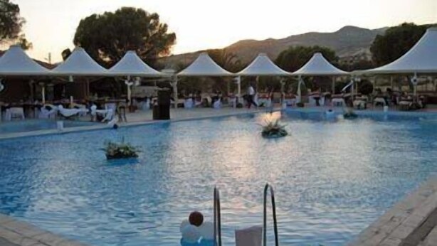 A swimming pool with lounge chairs and umbrellas, surrounded by trees and hills. - Berksoy Hotel (Bergama)