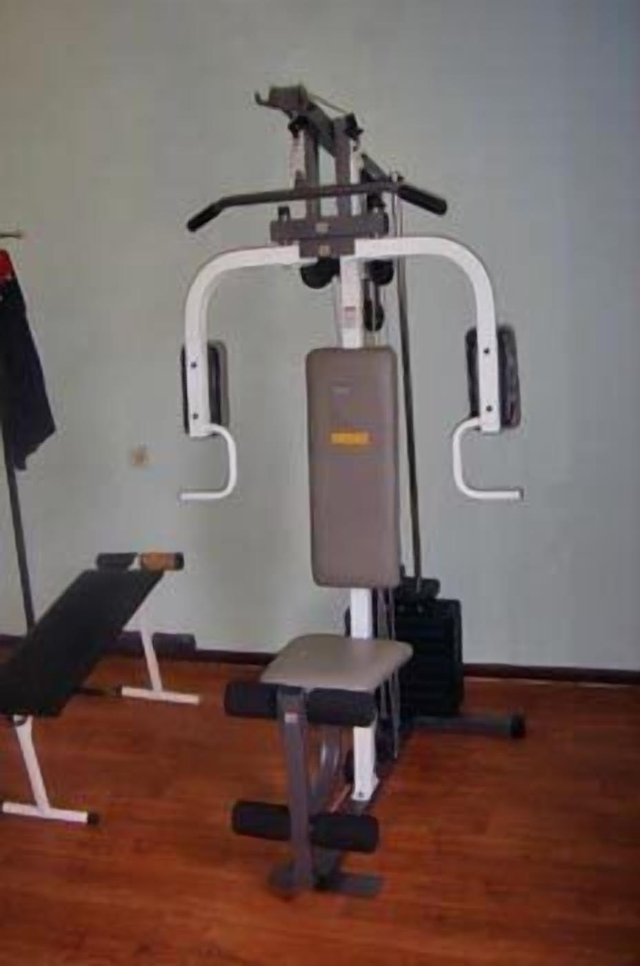 A gym with a bench, weight machine, and a wall-mounted rack.