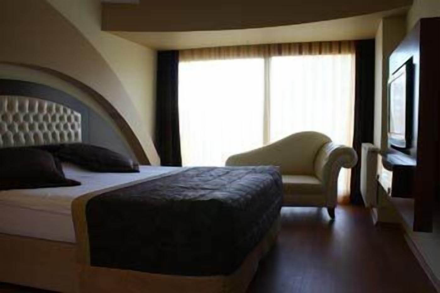 Una habitación de hotel con una cama, una silla, un ventanal grande y un televisor.