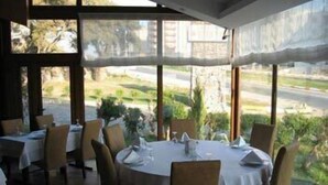 A restaurant with round tables and chairs, large windows with a view of greenery and a road. - Berksoy Hotel (Bergama)