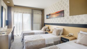 A hotel room with two beds, a desk, and a chair. There is a window with curtains, an air conditioning unit, and a painting on the wall. - Berksoy Hotel (Bergama)