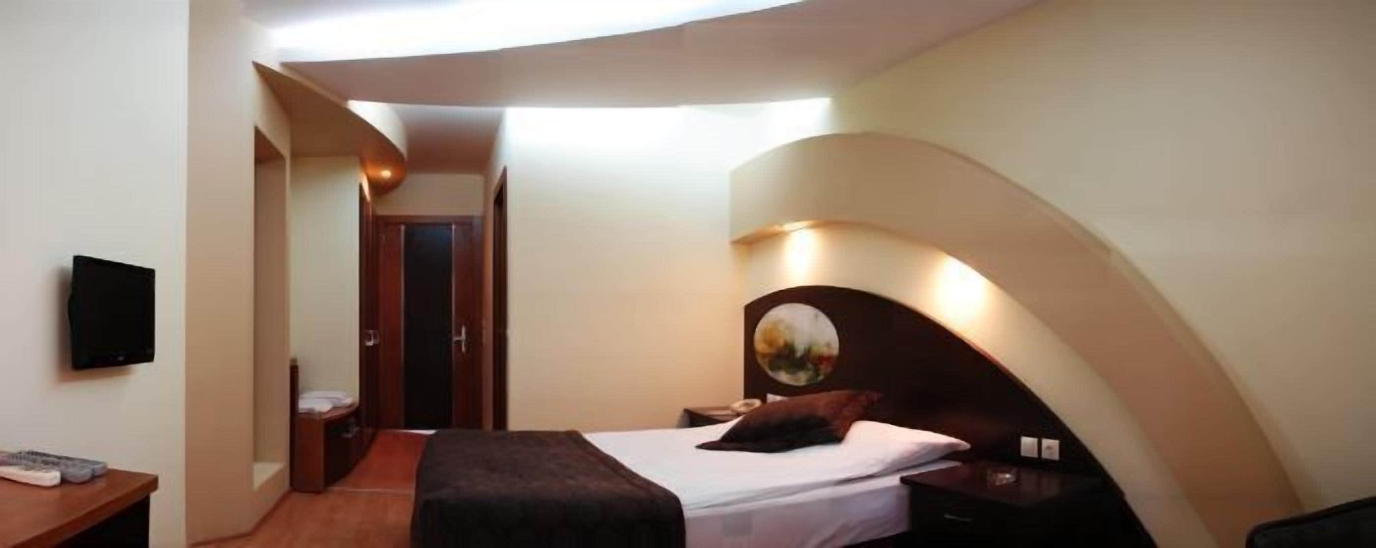Une chambre à coucher avec un plafond incurvé, un lit avec une tête de lit, une table de chevet et un téléviseur fixé au mur.
