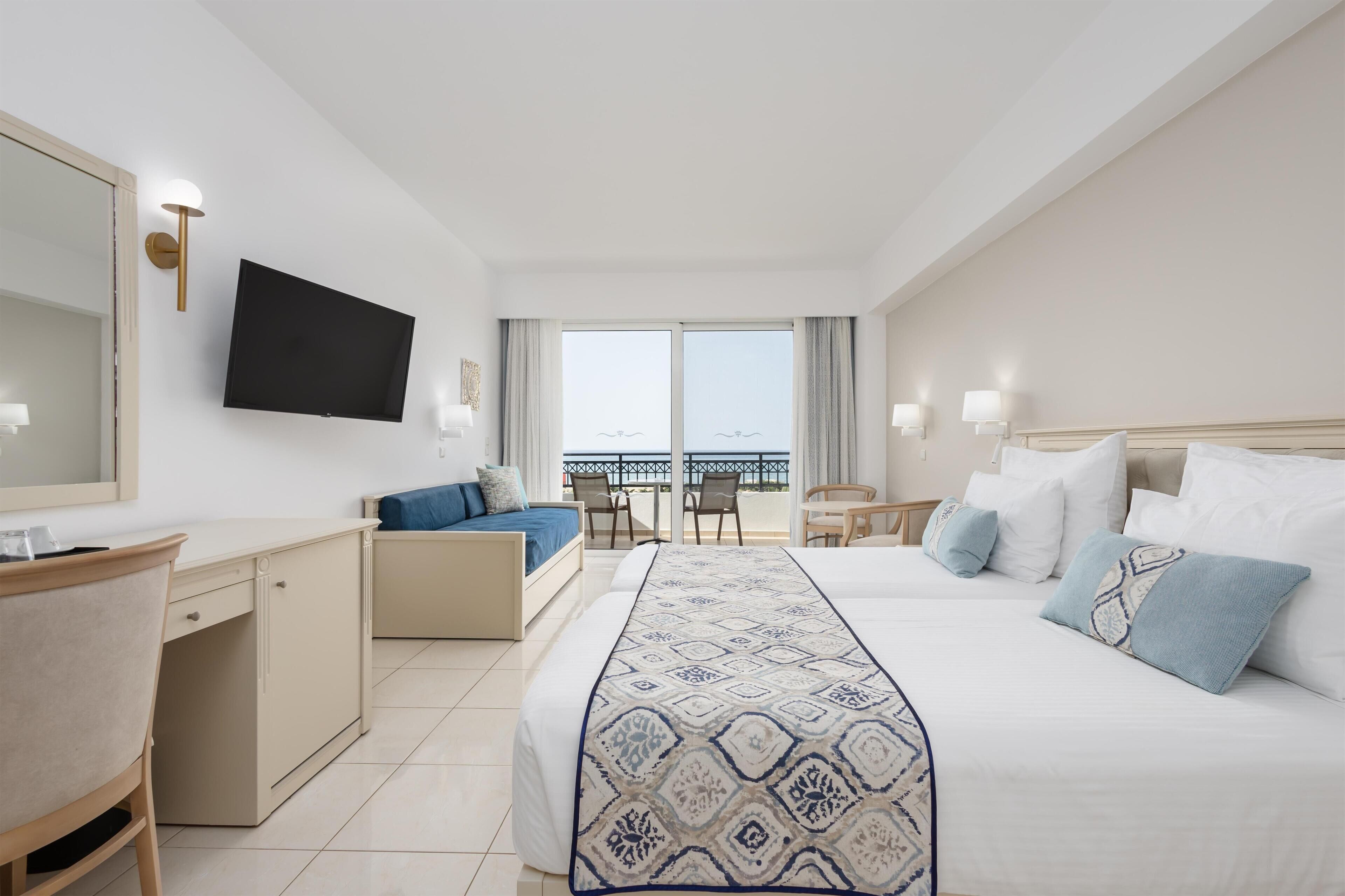 Habitación de hotel con cama, escritorio, silla, televisor y balcón con vistas.