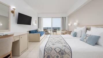 Habitación de hotel con cama, escritorio, silla, televisor y balcón con vistas.