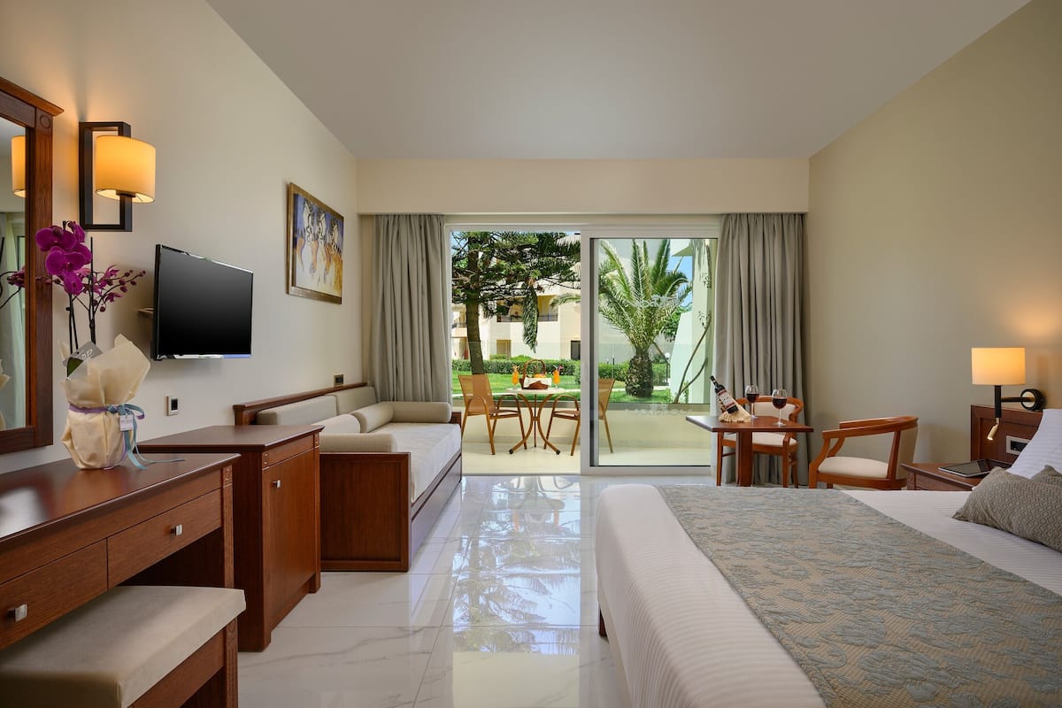 A hotel room with a bed, a desk, a chair, a TV, and a balcony with a table and chairs.