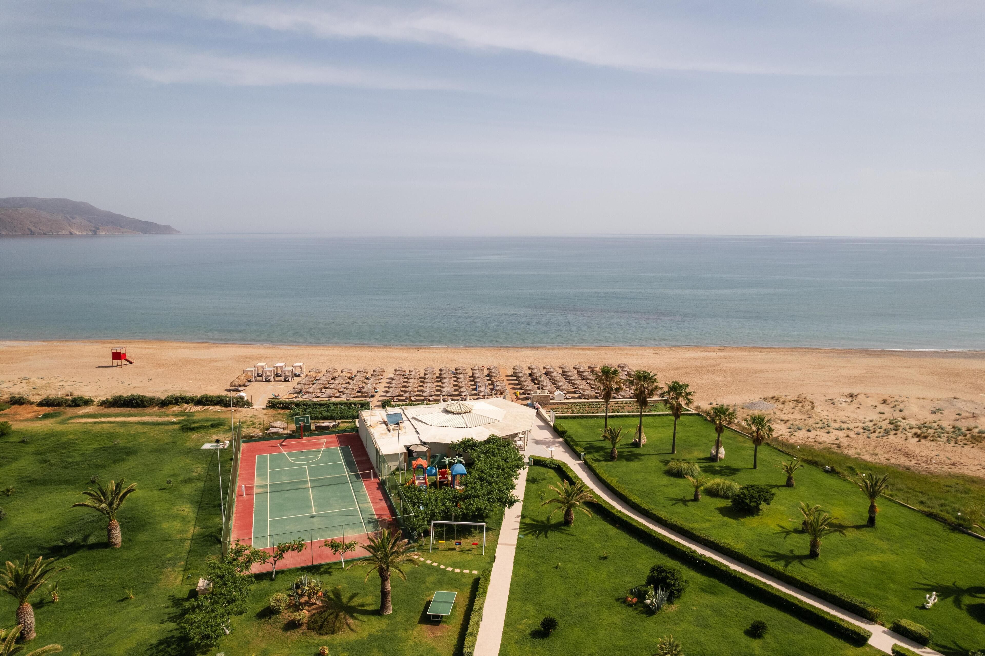 An aerial view of a coastal property with a tennis court, a pool area, and a beach.