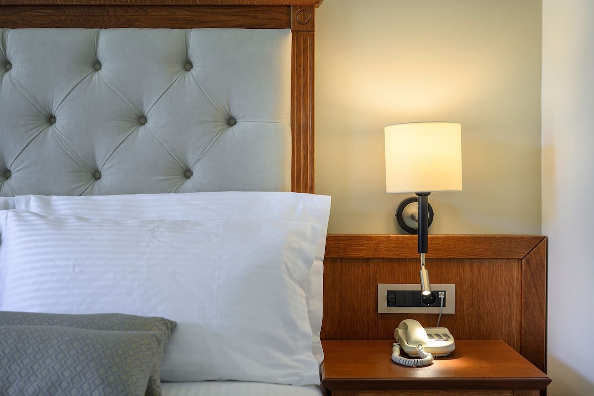 A hotel room with a tufted headboard, a bedside lamp, a telephone, and a power outlet.
