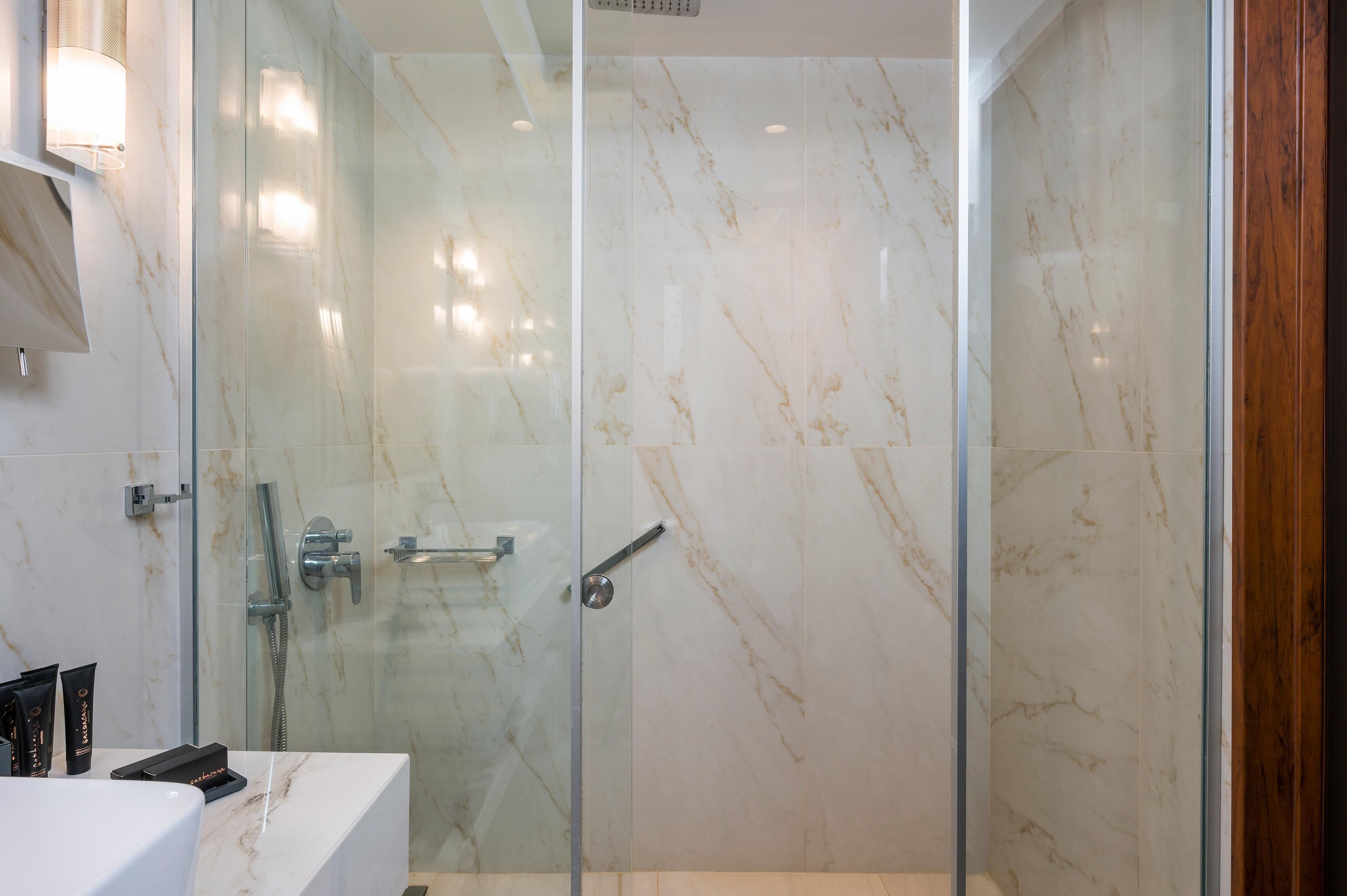 Un baño moderno con cabina de ducha de vidrio, paredes de mármol y un lavabo blanco.
