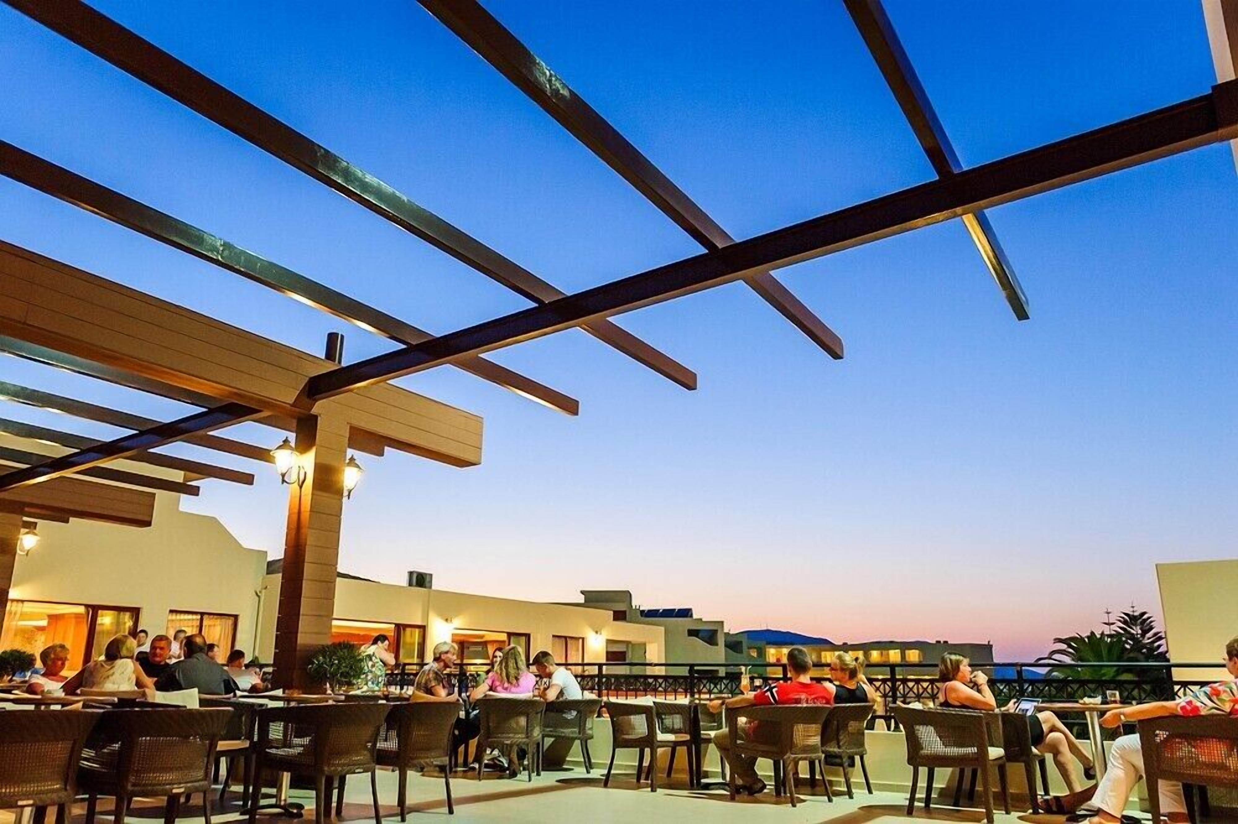 Un área de comedor al aire libre con mesas y sillas, una estructura de pérgola y vista al cielo.