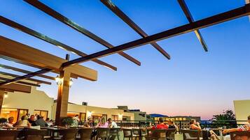 Un área de comedor al aire libre con mesas y sillas, una estructura de pérgola y vista al cielo.