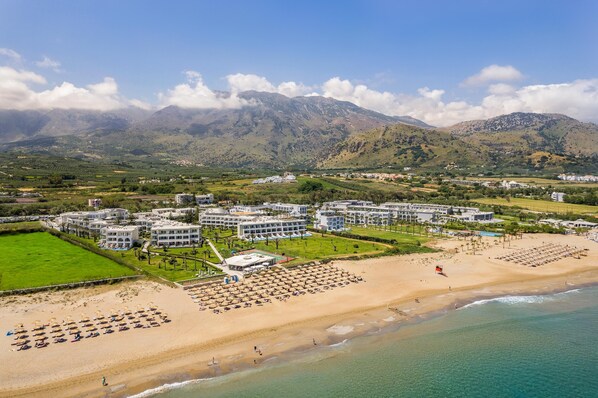 A resort with multiple buildings, a beach with sun loungers, and mountains in the background. - Vantaris Palace (Apokoronas)