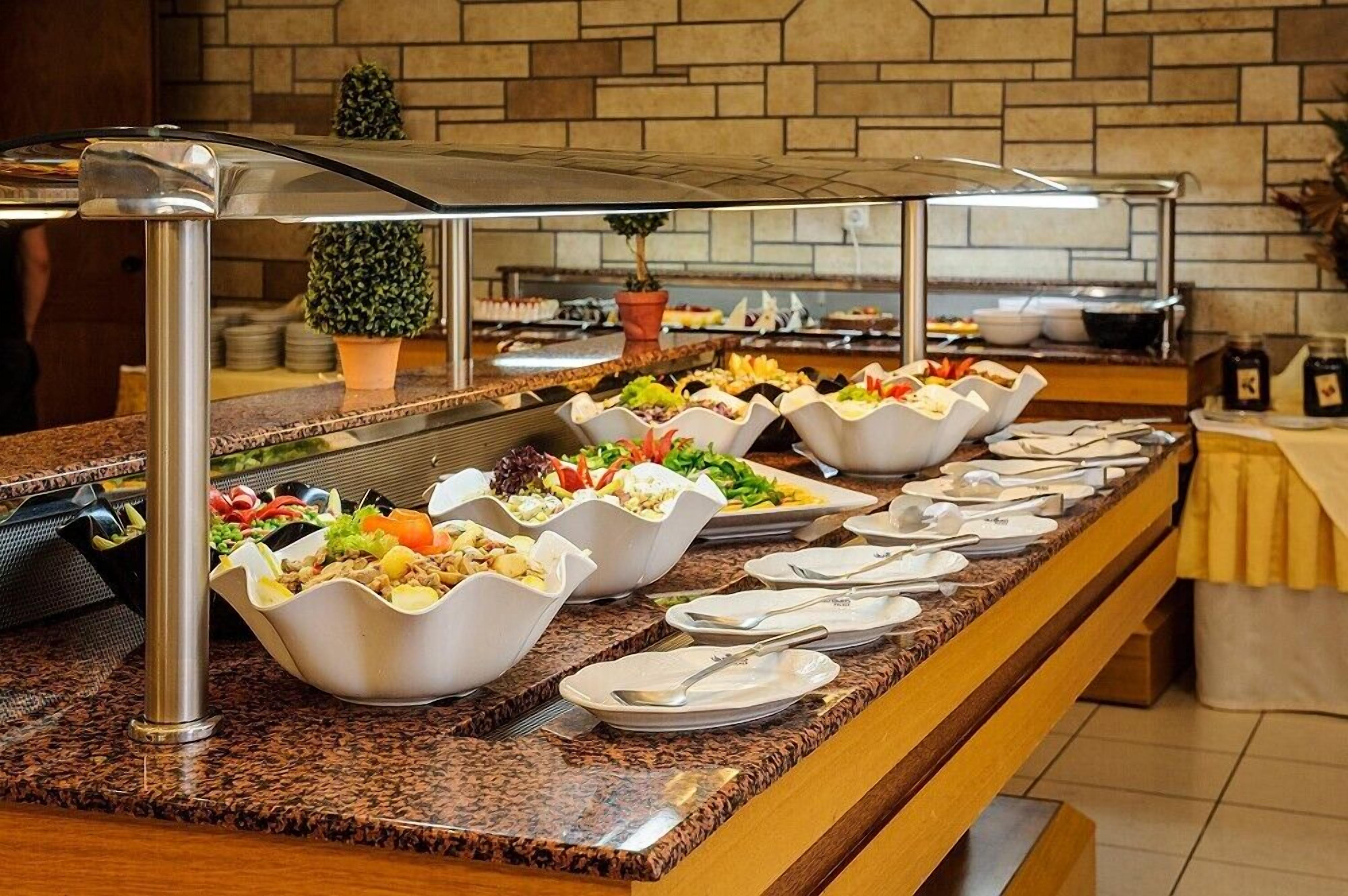 Un buffet proposant divers plats servis dans des bols blancs, avec un mur en pierre en arrière-plan et une plante en pot.