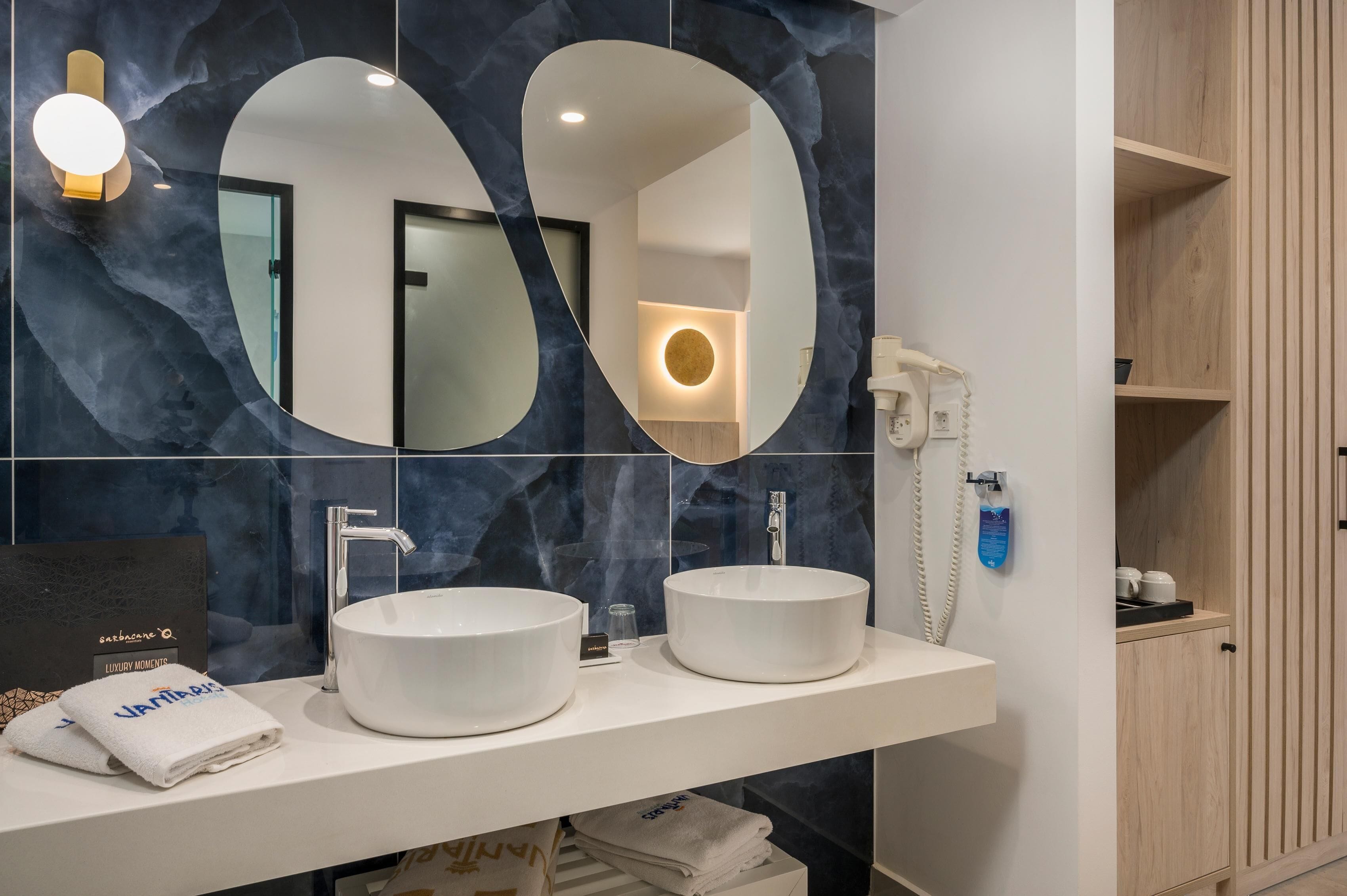 Une salle de bain moderne avec deux vasques rondes blanches, un grand miroir et un téléphone fixé au mur.