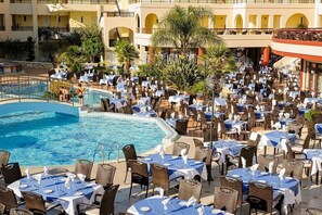 A poolside area with multiple tables and chairs, a swimming pool, and a building with balconies. - Vantaris Palace (Apokoronas)