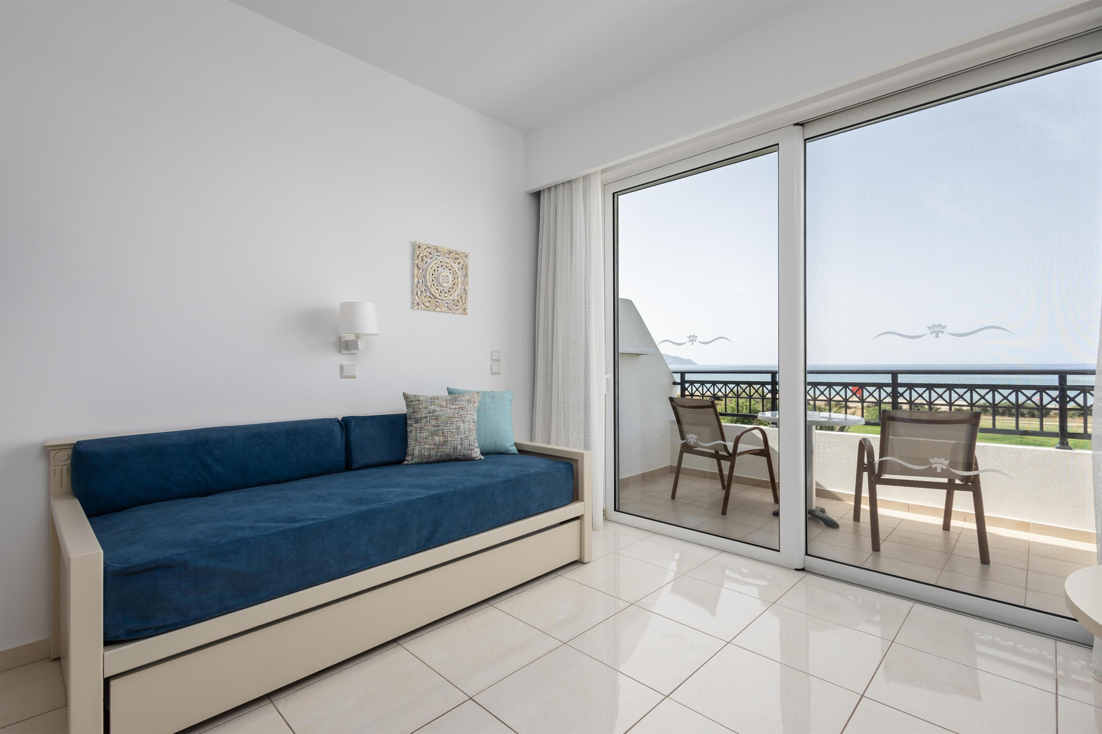 A room with a blue sofa, a small table, and a view through a glass door to an outdoor area with chairs and a railing.