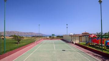 Una cancha de tenis al aire libre con superficie verde, rodeada por una valla y equipada con iluminación.