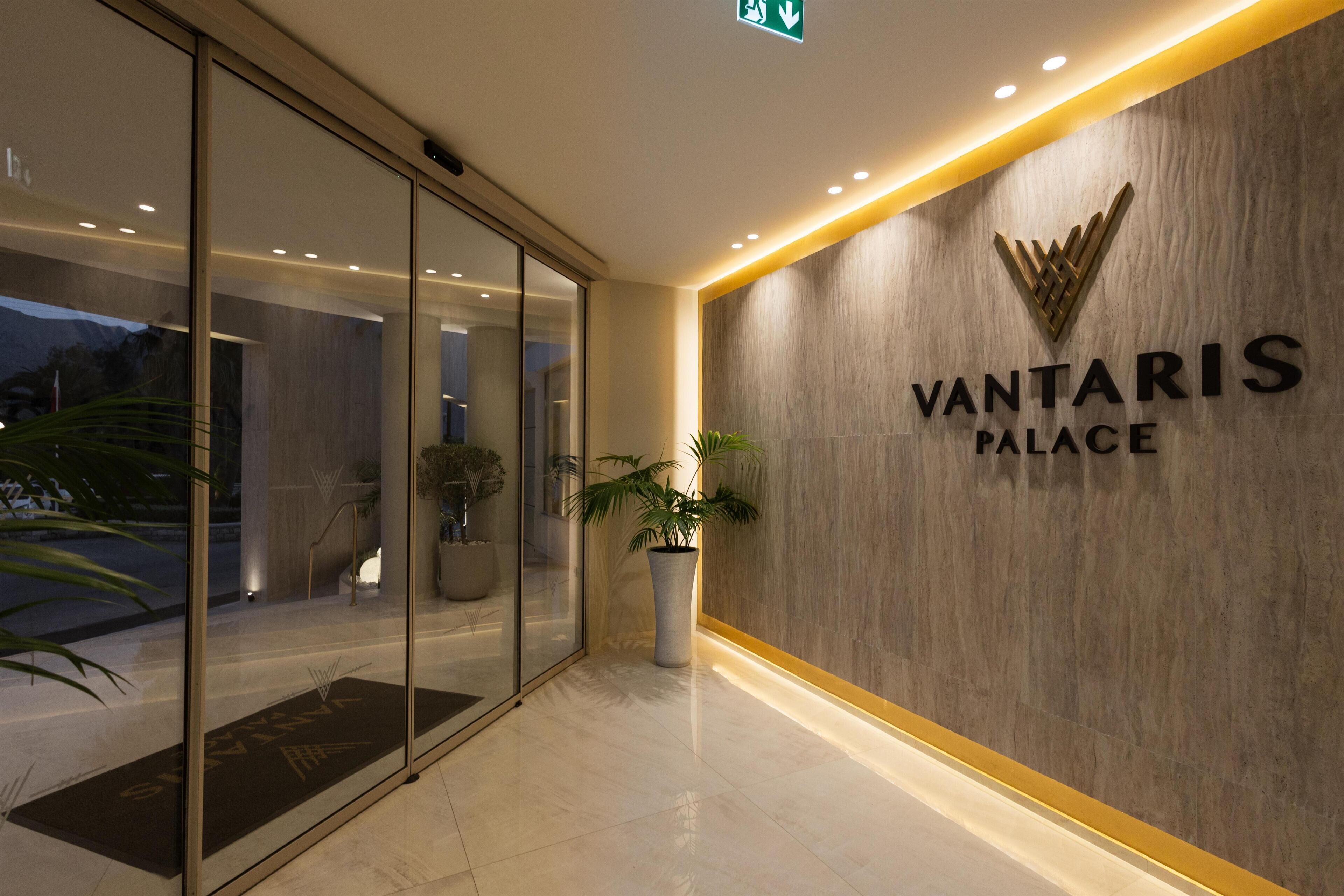 Uma entrada moderna com porta de vidro, planta em vaso e placa com a inscrição "VANTARIS PALACE".