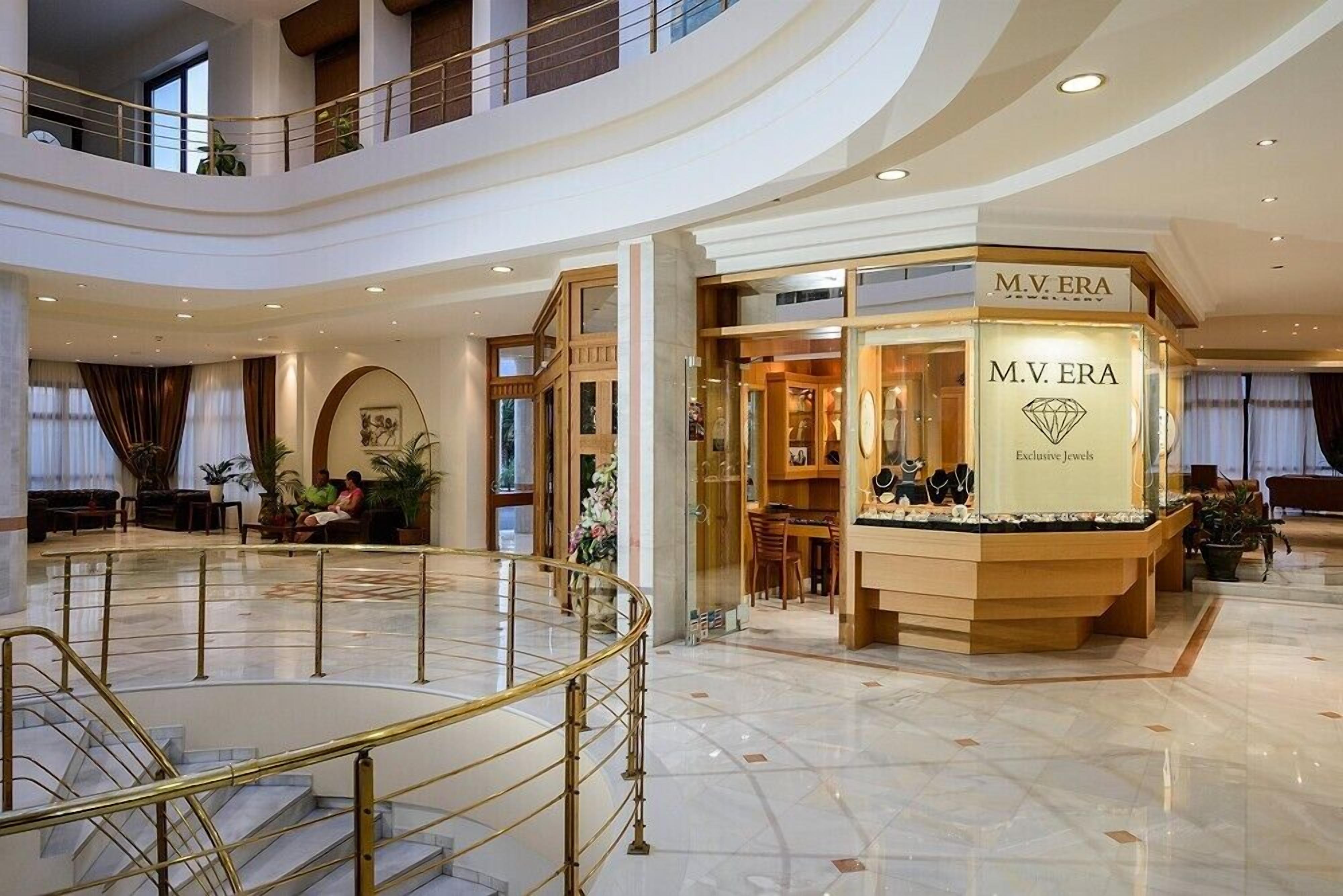 A spacious lobby with a central atrium, a M.V. ERA jewelry store, and a staircase leading to an upper level.