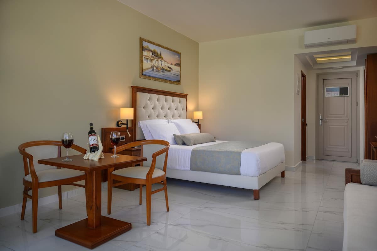 A hotel room with a bed, a dining table with chairs, a painting on the wall, and an air conditioning unit.