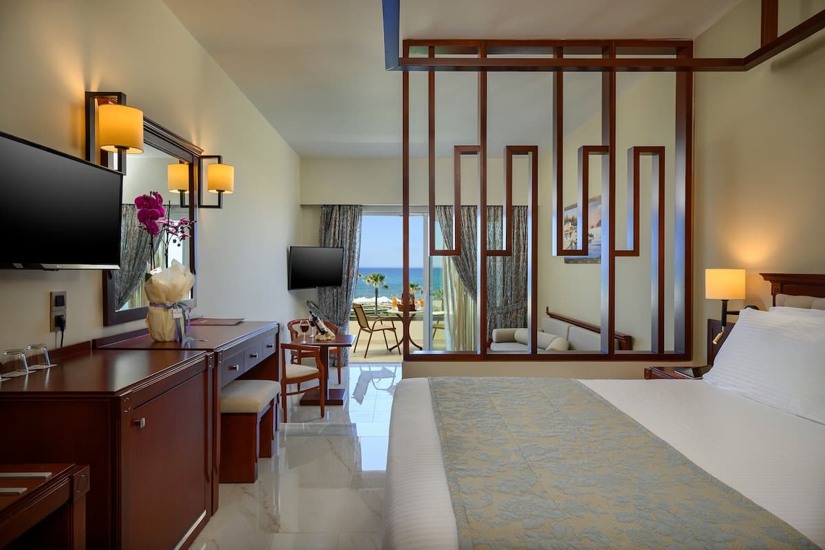 A hotel room with a bed, a desk, a television, and a view of the ocean.