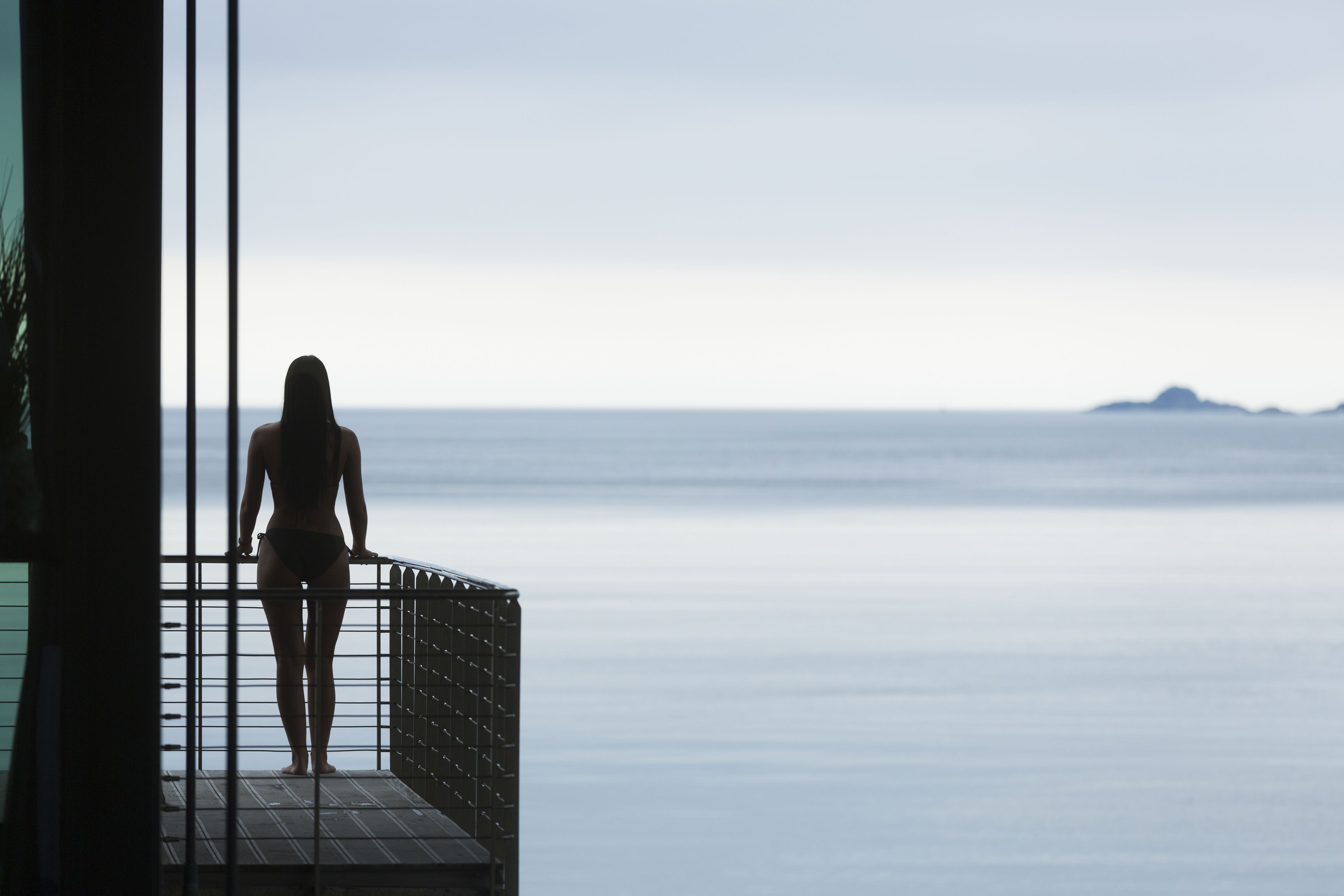 A person standing on a balcony overlooking a calm sea.