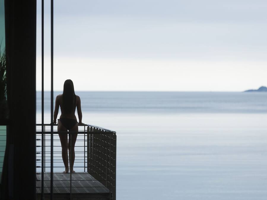 A person standing on a balcony overlooking a calm sea.