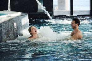 Un couple se détend dans un bain à remous équipé de jets, entouré d’un intérieur moderne avec de grandes fenêtres.